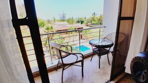 Un balcone con due sedie e un tavolino, affacciato su una piscina e del verde.