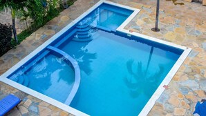 Una piscina rettangolare con bordi in pietra, circondata da palme e un muro in pietra.