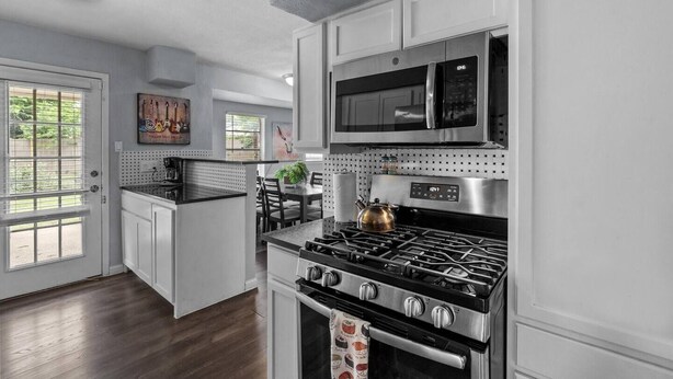 Una cucina con mobili bianchi, un piano cottura in acciaio inossidabile, un forno a microonde e un'area pranzo con tavolo e sedie.