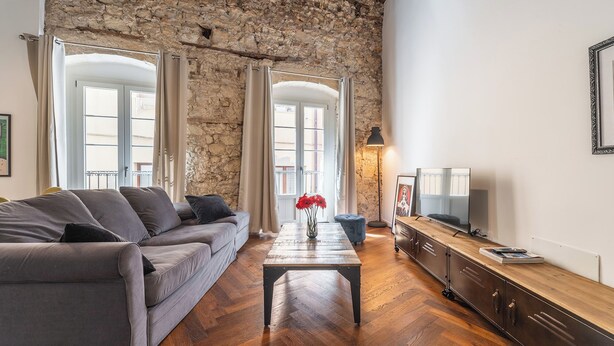 Ein Wohnzimmer mit einer Steinsäule, einem Sofa, einem Couchtisch, einem Fernseher und einer Lampe.