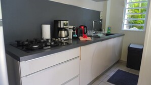 A kitchen with a gas stove, coffee maker, kettle, and a small trash bin. - MOOREA - Waterfall Pool Coconut 1 (Pihaena)