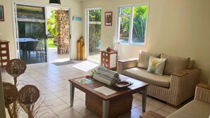 A living room with a sofa, a coffee table, and a dining area with a table and chairs. - MOOREA - Waterfall Pool Coconut 1 (Pihaena)