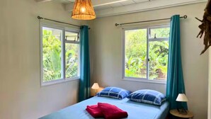 A bedroom with two windows, a bed with blue and red pillows, a hanging lamp, and curtains.