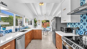Una cocina moderna con armarios blancos, un lavavajillas de acero inoxidable, un microondas negro y una estufa a gas.