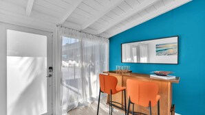 Una habitación con un escritorio de madera, dos sillas naranjas, un espejo grande y una pared azul.