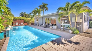 Una piscina con agua cristalina azul, rodeada de palmeras y un patio con mobiliario exterior.