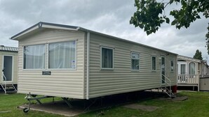 A single-story mobile home with a flat roof, large windows, and a small porch. - Cabin - Sleeps 6 - Beach 10 Minutes Drive (Clacton-on-Sea)