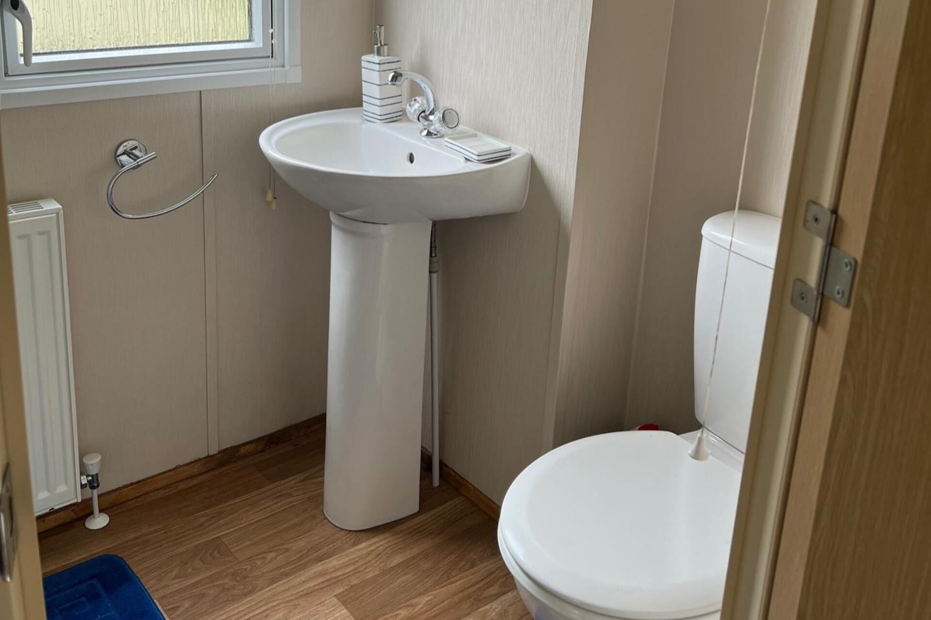 A small bathroom with a pedestal sink, a toilet, and a window.