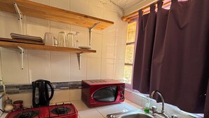 Eine kleine Küche mit Gaskochfeld, Mikrowelle, Spüle und einem Fenster mit Vorhängen.