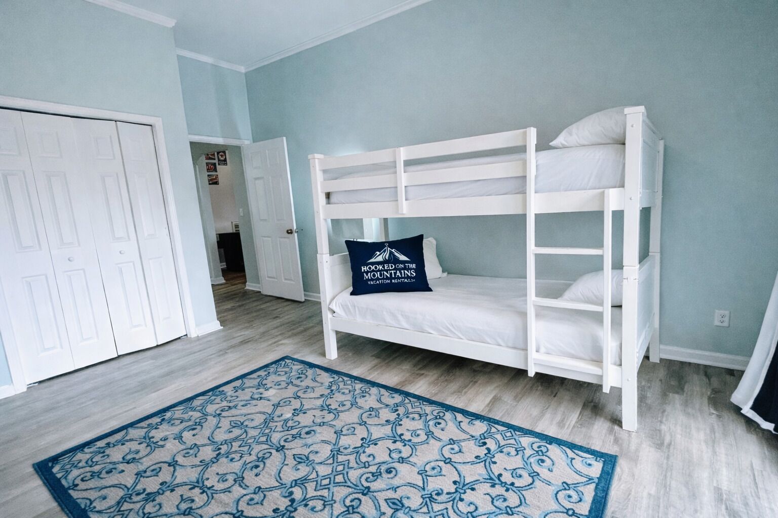 Une chambre avec un lit superposé, un tapis bleu à motifs, une porte et un couloir.