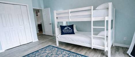Une chambre avec un lit superposé, un tapis bleu à motifs, une porte et un couloir.