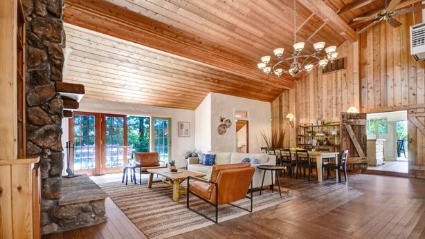 Amplia sala de estar con chimenea de piedra, techo de madera y comedor con mesa y sillas.