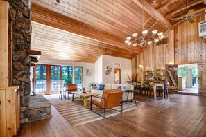 Un vaste espace de vie doté d’une cheminée en pierre, d’un plafond en bois et d’un coin repas avec une table et des chaises.