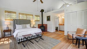 Un dormitorio con una cama a cuadros, una chimenea, un ventilador de techo y vistas al baño.