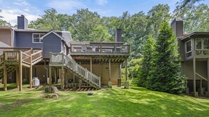 Ein zweistöckiges Haus mit überdachter Veranda, Holzterrasse und gepflegtem Rasen.