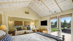 Ein Schlafzimmer mit einem großen Bett, einem Schreibtisch und einem Fernseher. Eine Glastür führt auf eine Terrassenförmige Außensitzgelegenheit.