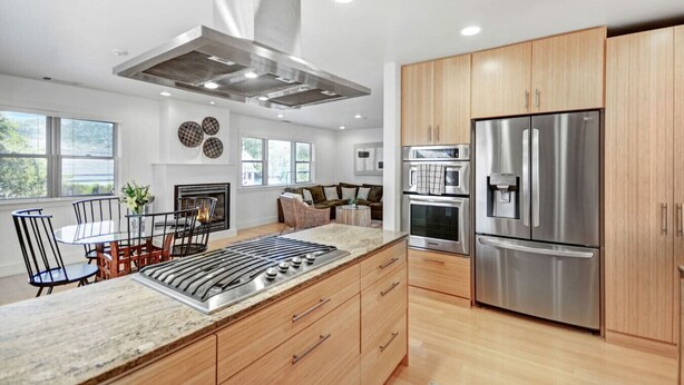 A modern kitchen with a central island, stainless steel appliances, wooden cabinets, and a dining area with a fireplace.