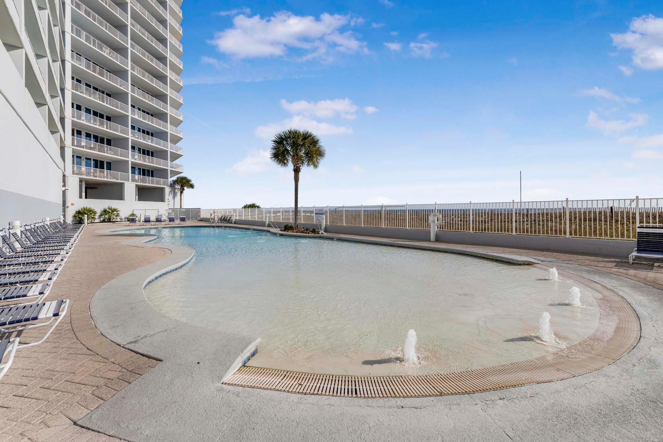 A swimming pool with a curved edge, surrounded by lounge chairs and a palm tree.
