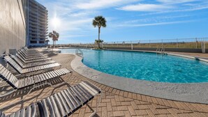 A poolside area with lounge chairs and a clear blue pool, surrounded by a fence and palm trees. - Lighthouse 1416 (Gulf Shores)