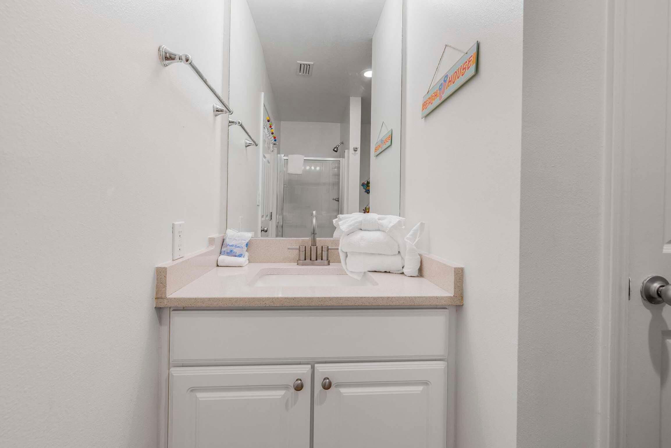 Un baño con lavamanos, espejo, toallero y una puerta que da a la ducha.