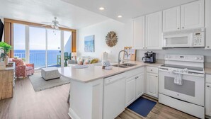 A modern kitchen with white cabinets, a built-in oven, and a microwave. There is a large window offering a view of the ocean. - Lighthouse 1416 (Gulf Shores)