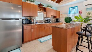Une cuisine moderne avec des meubles en bois, un réfrigérateur en acier inoxydable, un plan de travail en granit et un coin bar avec des tabourets.