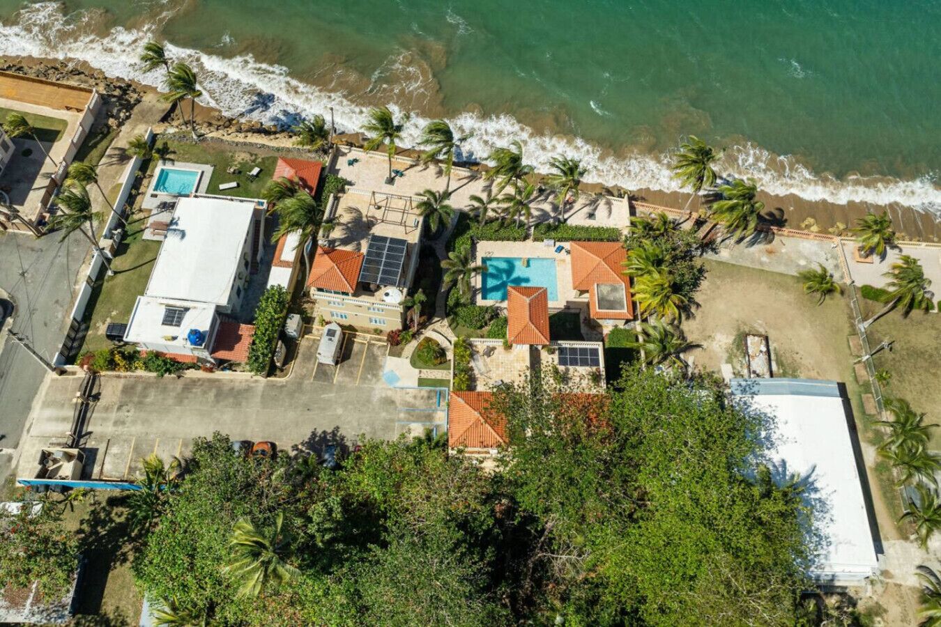 Vista aérea de una propiedad costera con varias edificaciones, una piscina y una playa.