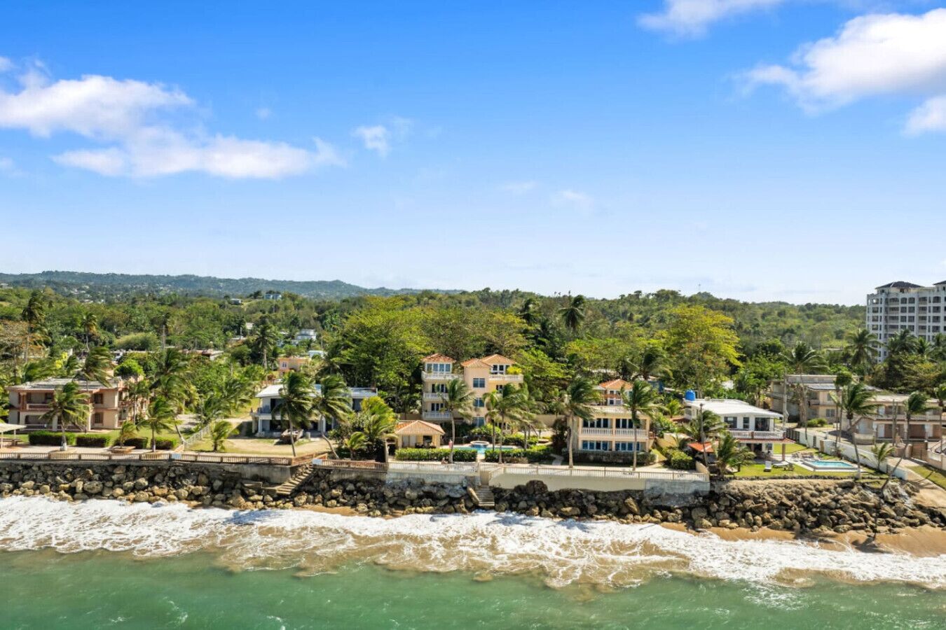 A coastal residential area with houses, a rocky shoreline, and a view of the ocean.