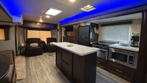 A compact RV kitchen with a central island, built-in appliances, and a seating area with a sofa and chairs.
