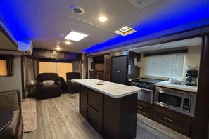 A compact RV kitchen with a central island, built-in appliances, and a seating area with a sofa and chairs.