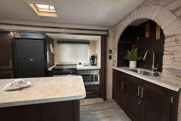 A compact kitchen with a central island, a built-in oven, and a sink under a stone archway. - RIncon Camper Retreat (Rincón)