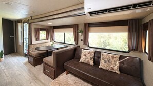 A cozy RV interior with a dining area, a sofa, and large windows.