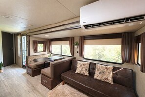 A cozy RV interior with a dining area, a sofa, and large windows.