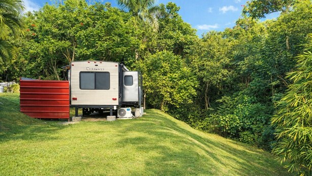 A mobile home with a Chevrolet logo, parked on a grassy slope surrounded by dense greenery.