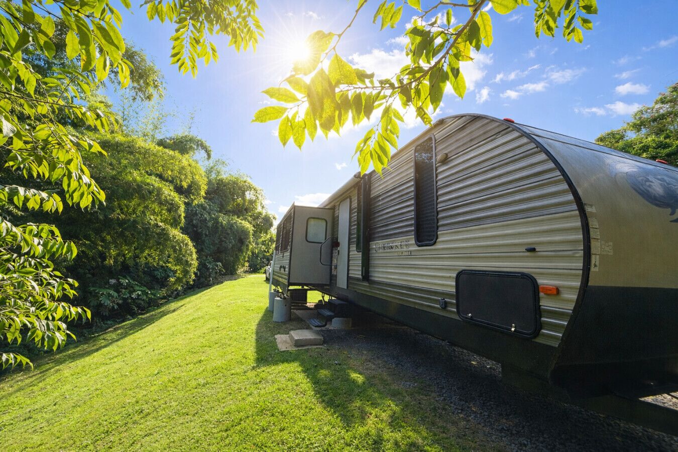 A recreational vehicle parked in a grassy area with trees and a clear sky.