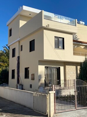 A modern two-story building with a balcony, a gated entrance, and a clear sky.