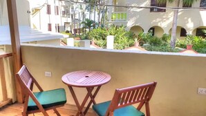A balcony with a round wooden table and two wooden chairs with green cushions. - Cabarete Center 2 BR Condo with a Cozy Terrace (Cabarete)