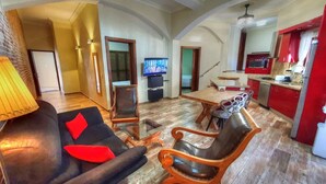 A living room with a sofa, a coffee table, and a TV. There is a kitchen area with red cabinets and a dining table. - Cabarete Center 2 BR Condo with a Cozy Terrace (Cabarete)