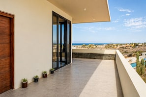 Un balcon moderne donnant sur la mer, agrémenté de plantes en pot et doté d’une porte en bois.