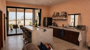 Cozinha moderna com área de bar, espaço de refeições com sofá e vista pelas portas de vidro.
