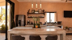 Uma cozinha moderna com uma ilha central, banquetas, uma geladeira e uma TV de tela plana.