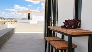 Um pátio moderno ao ar livre com mesa e bancos de madeira, um vaso de planta e vista para um edifício branco e paisagem.