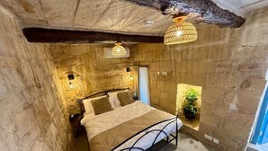 Ein Schlafzimmer mit Steinsandsteinwand, einem Bett, einer hängenden Leuchte und einem kleinen Fenster mit Pflanze.