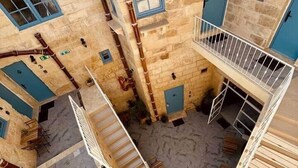 Ein mehrstufiger Innenhof mit Steinmauern und blauen Fensterrahmen, mit Treppen und Sitzgelegenheiten im Freien.
