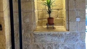 Un muro de piedra con una pequeña ventana, una planta en maceta y un cuadro enmarcado.