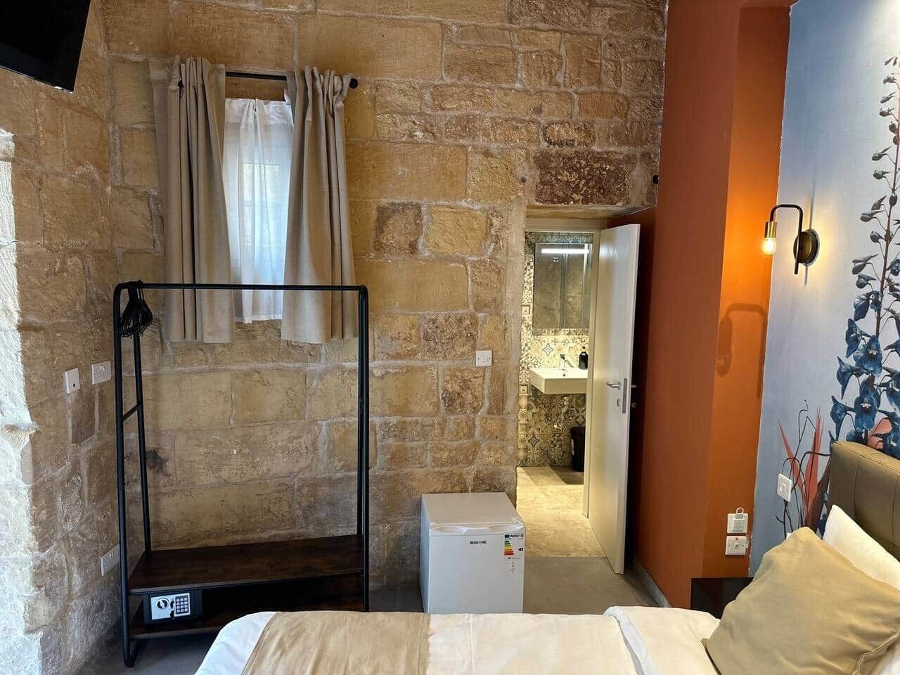 Una habitación con literas, un electrodoméstico blanco pequeño, un baño con espejo y una pared con un mural de plantas.