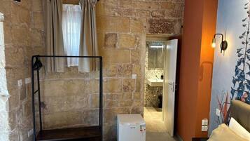 Una habitación con literas, un electrodoméstico blanco pequeño, un baño con espejo y una pared con un mural de plantas.