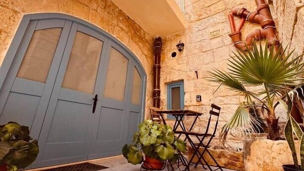 Un patio con una puerta azul, una mesita, sillas y plantas en macetas.