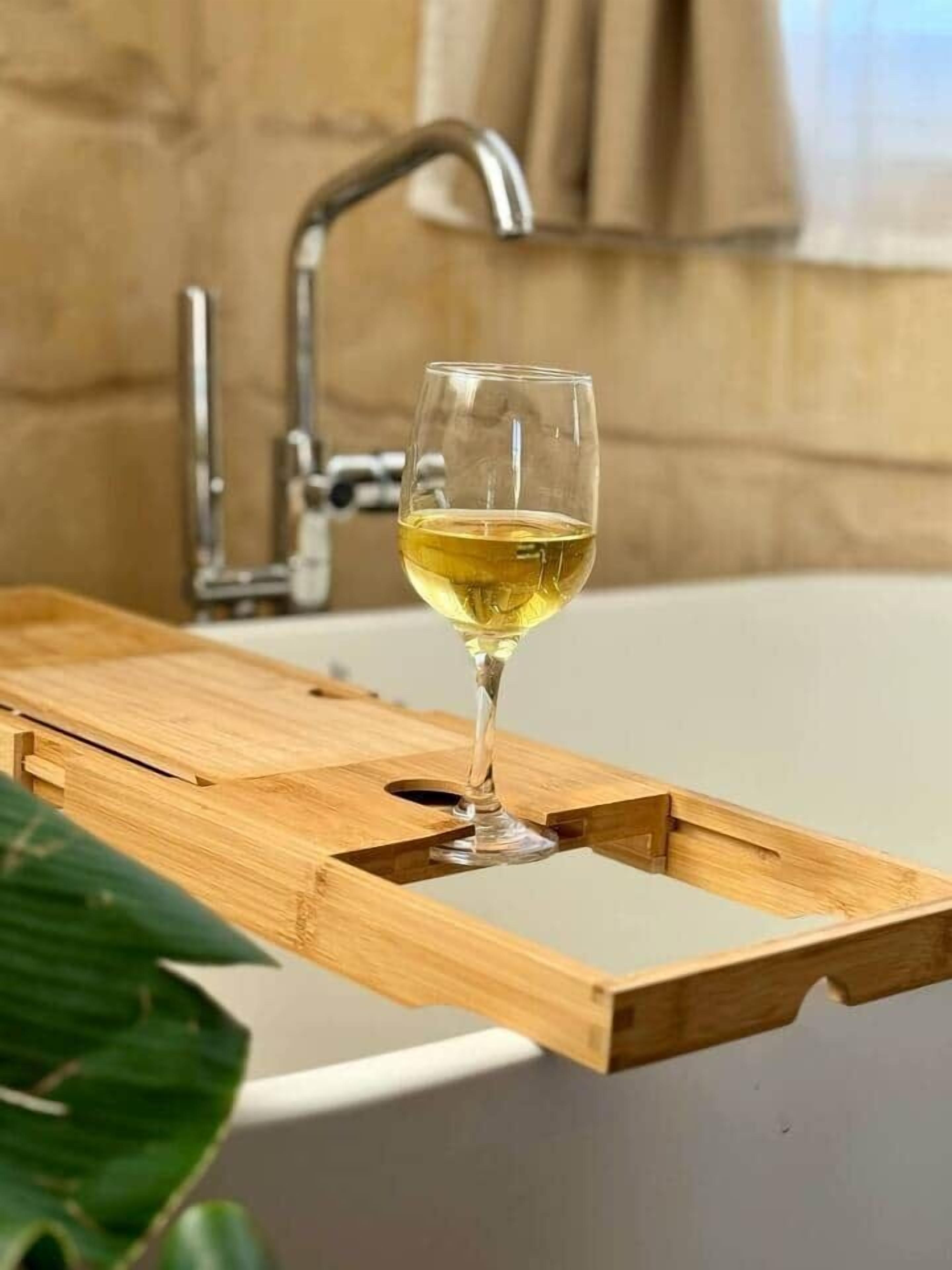 Una copa de vino blanco sobre una bandeja de madera, junto a una bañera.