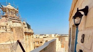 A narrow corridor with stone walls, a metal railing, and a view of buildings in the distance. - Kappella Boutique - Room 4 (Zurrieq)